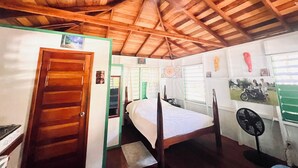 A room with a wooden ceiling, a bed, a door, and a fan. - Charming beachfront studio cabana in sunny Placencia (Placencia)