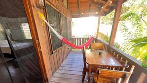 A wooden deck with a table and chairs, a hammock, and a window with metal bars. - Charming beachfront studio cabana in sunny Placencia (Placencia)