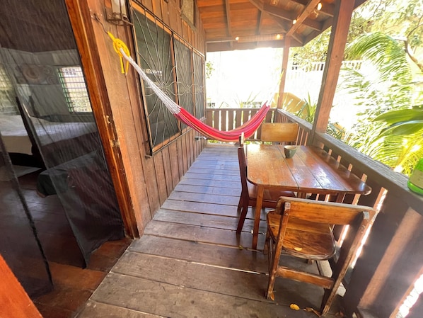 Une terrasse en bois avec une table et des chaises, un hamac et une fenêtre avec des barreaux en métal.