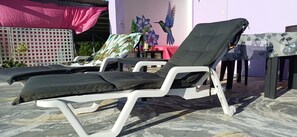 A poolside area with lounge chairs, a table, and a wall with a floral mural. - Ocean View Terrace Retreat Caribbean Escape (Buccoo)