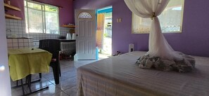 A room with a bed, a table, a chair, a window, a door, and a view of the outside. - Ocean View Terrace Retreat Caribbean Escape (Buccoo)