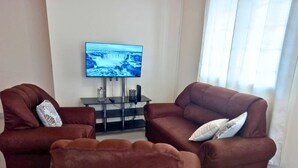 Un salon avec deux canapés marron, un téléviseur posé sur un meuble et une fenêtre avec des rideaux.