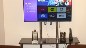 Un téléviseur à écran plat fixé au mur, une télécommande, un objet décoratif et une bouteille posée sur une table en dessous.
