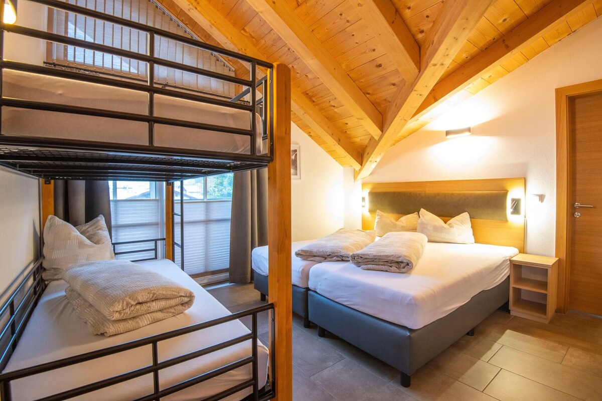A hotel room with a bunk bed, a single bed, and a wooden ceiling.