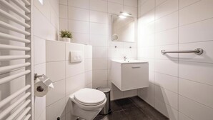 A small, modern bathroom with white tiles, a toilet, a sink, a mirror, and a towel rack. - Holiday Home in De Koog Near Beach (De Koog)