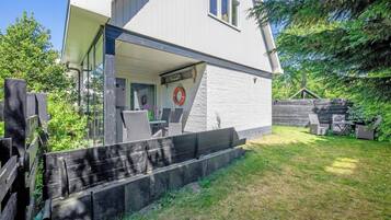 Una casa moderna con un área de estar cubierta al aire libre, una cerca de madera y un patio con césped.