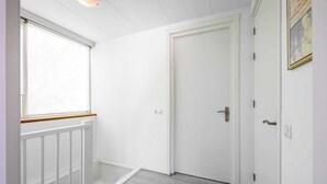 A hallway with a white door, a window with a wooden frame, and a light switch on the wall. - Holiday Home in De Koog Near Beach (De Koog)