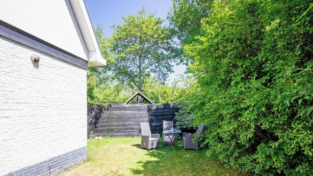 A backyard with a white building, a wooden fence, and a small shed. There are two chairs and a table in the yard. - Holiday Home in De Koog Near Beach (De Koog)