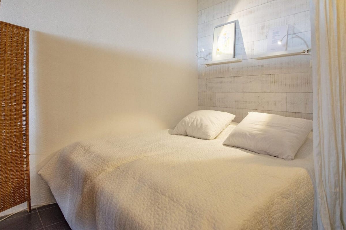 A bedroom with a bed, pillows, a headboard with a picture, and a wicker side table.