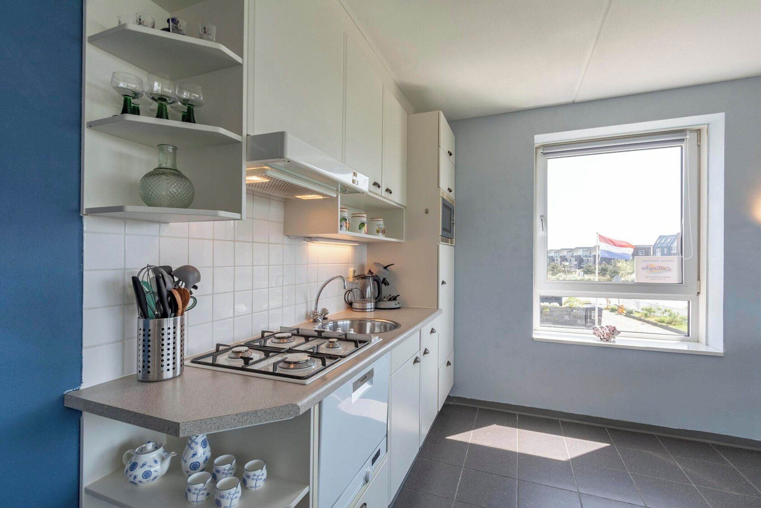 A modern kitchen with white cabinets, a gas stove, and a window with a view of buildings.