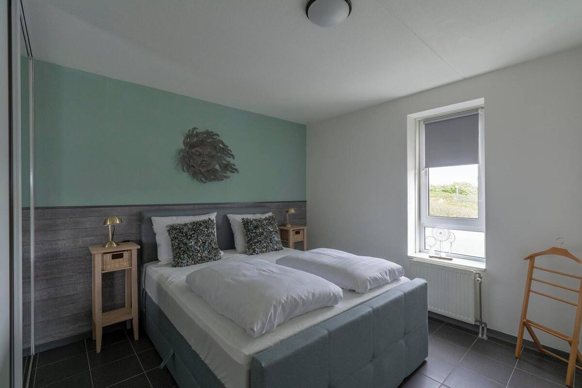 A bedroom with a bed, bedside tables, a wall decoration, a window, and a radiator.