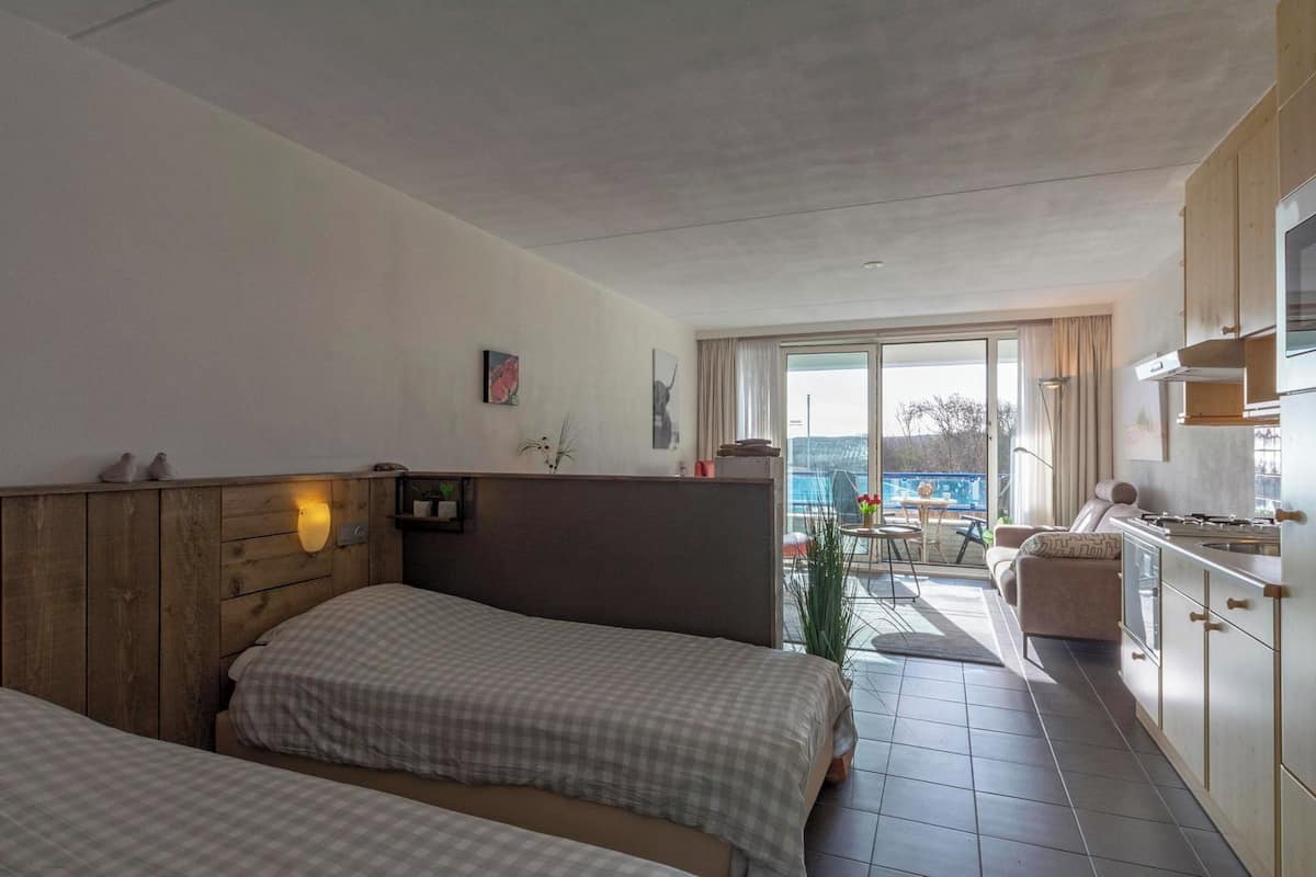 A hotel room with two beds, a kitchenette, a dining area, and a view of the outdoors.
