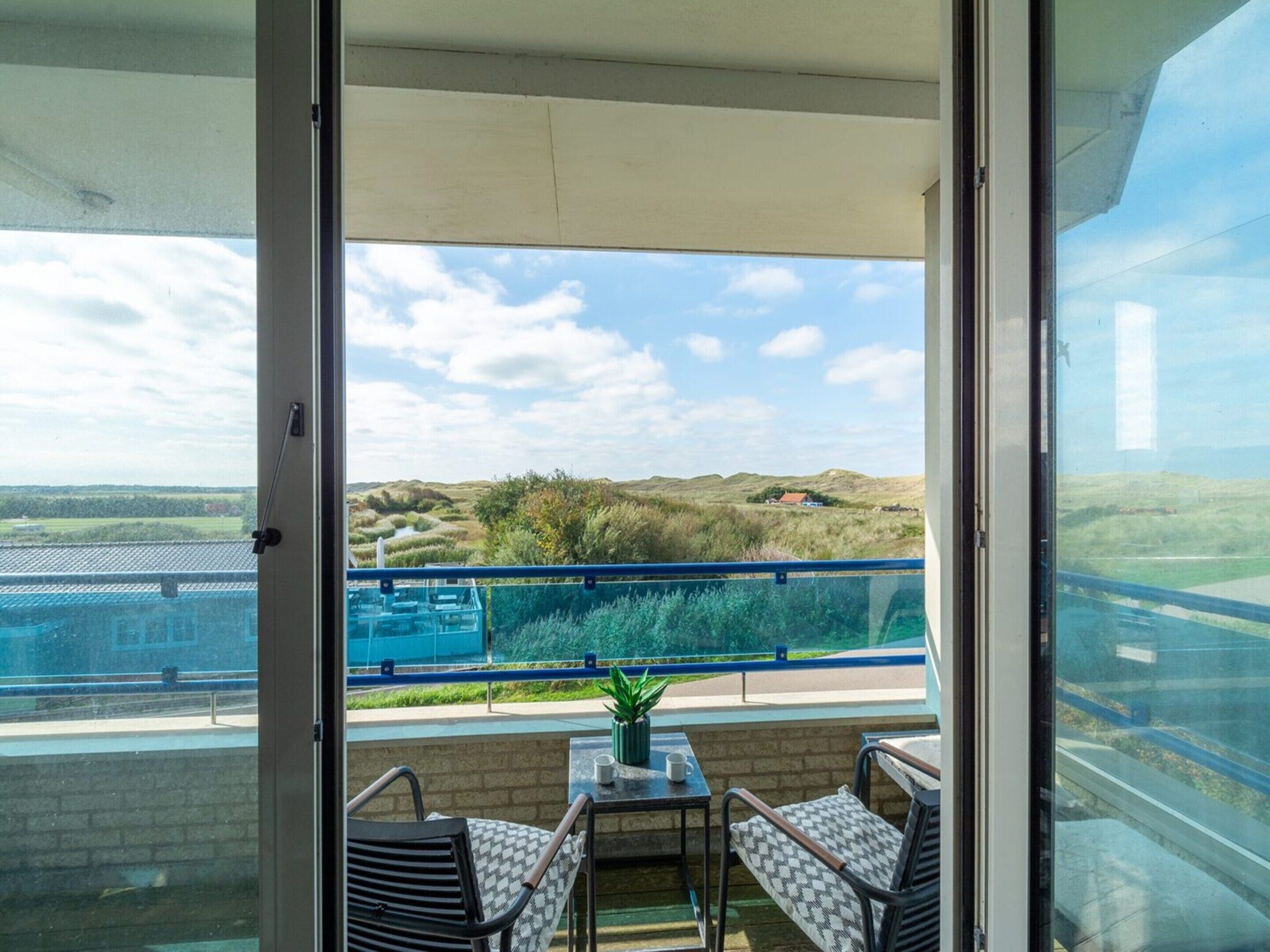 A balcony with a view of a landscape, a table with chairs, and a small plant.