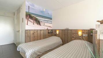 Habitación con dos camas, cabecera de madera, un mural con motivos playeros y una pequeña estantería con una planta.