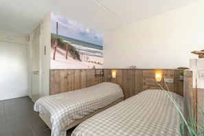 A room with two beds, a wooden headboard, a beach mural, and a small shelf with a plant. - Studio in Groote Keeten by the Beach (Callantsoog)