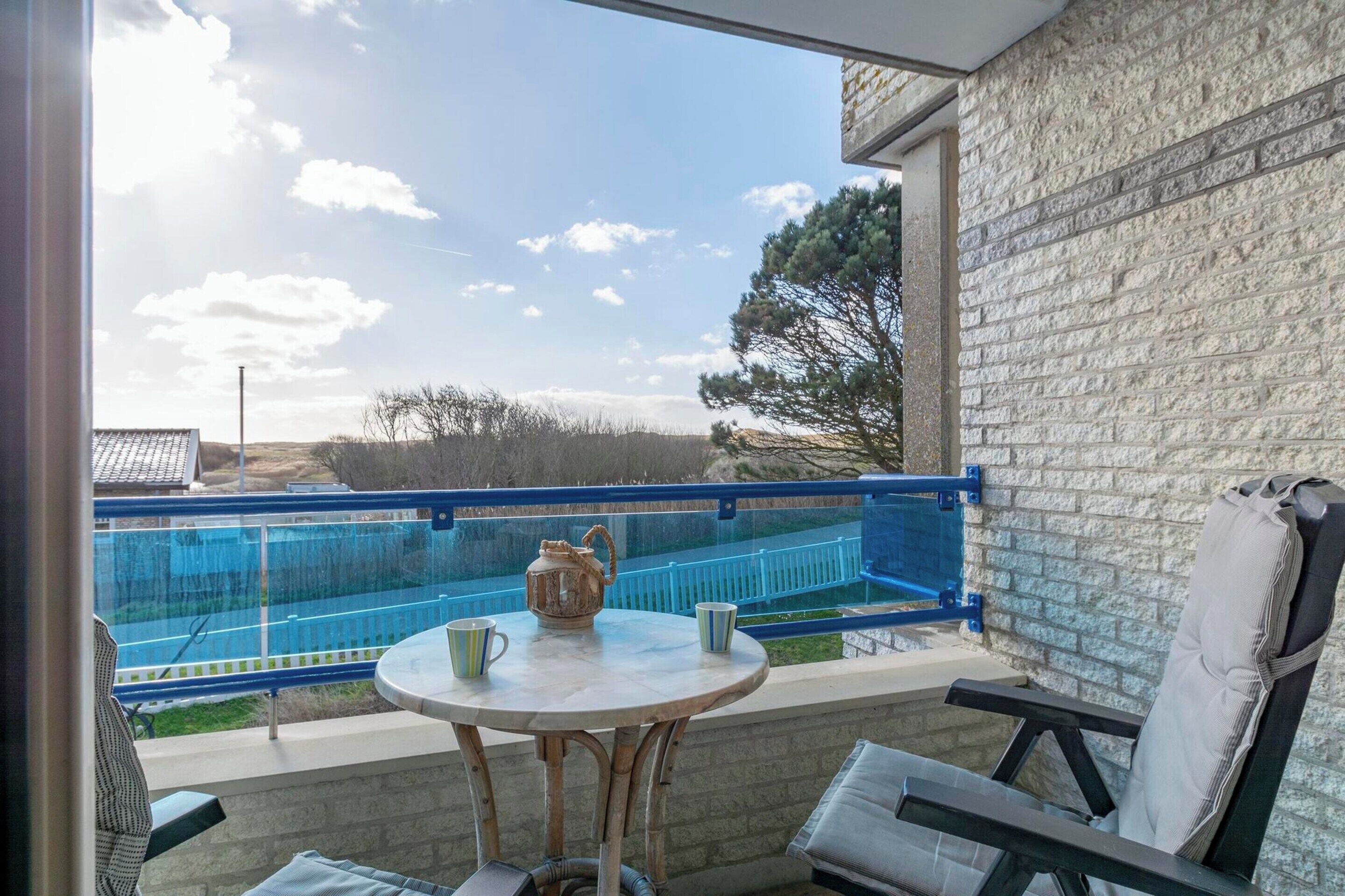 A balcony with a view of a swimming pool, a table with a teapot and cups, and a chair.
