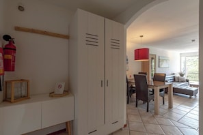 A room with a white wardrobe, a dining table with chairs, a sofa, and a red pendant light. - Wijde Blick 301 Adults Only Apartment (Callantsoog)