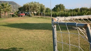 Una portería de fútbol con red, un campo de césped y un vehículo rojo al fondo.