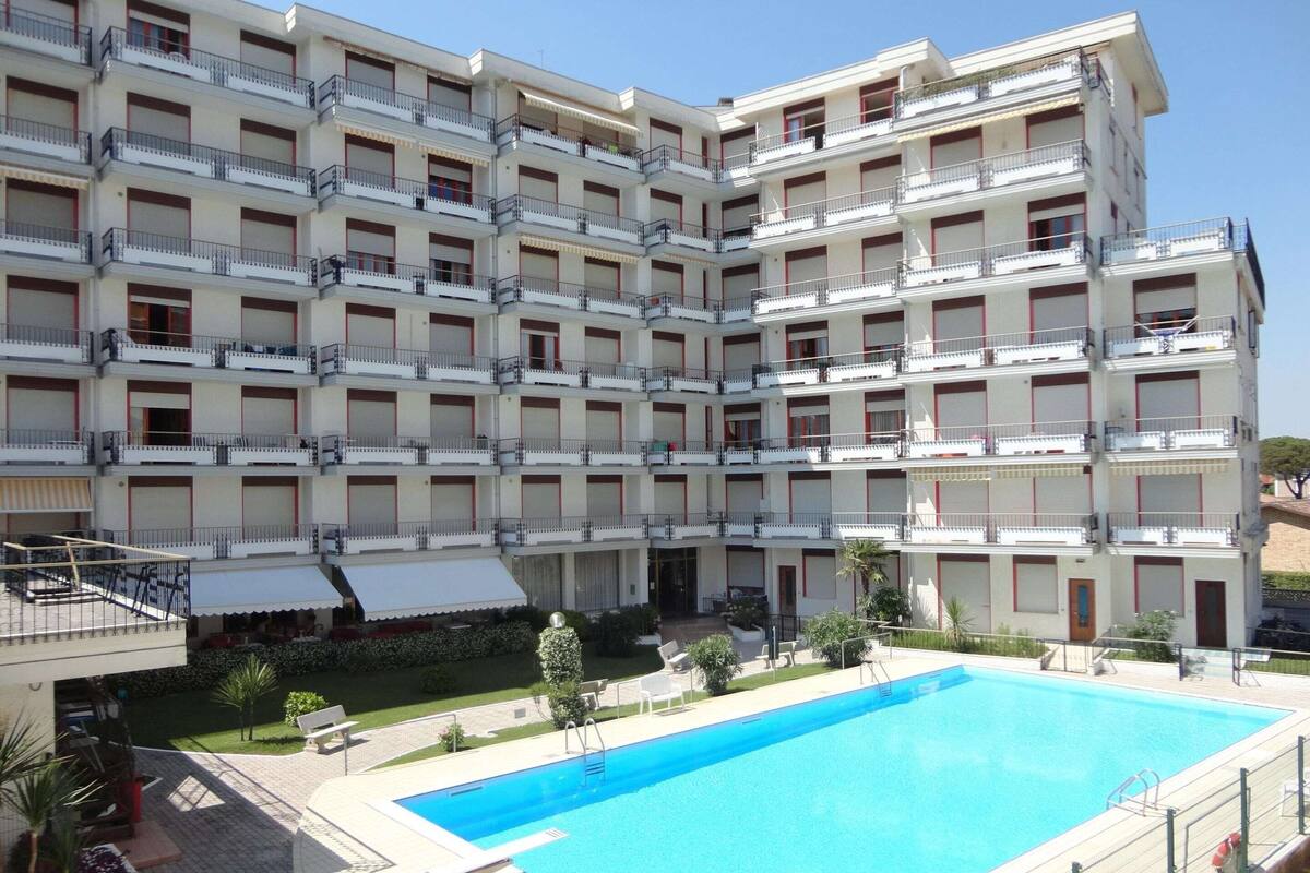 Un hotel de varios pisos con balcones, piscina y jardín.
