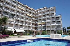 Un hotel de varios pisos con balcones, piscina y jardín.