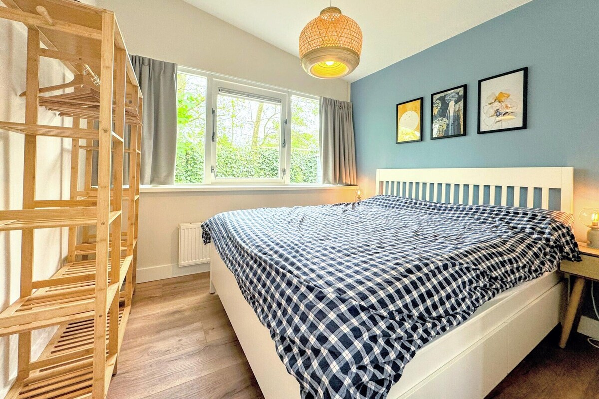 A bedroom with a bed, a wooden crib, a window with curtains, and a hanging light fixture.