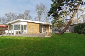 A modern house with a brick exterior, a large glass door entrance, and a patio with outdoor furniture. - Bungalow in Sint Maartenszee With Garden Views (Sint Maartensvlotbrug)