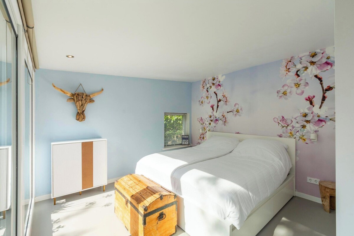 A bedroom with a bed, a wooden chest, a wall-mounted cow head, and a window.
