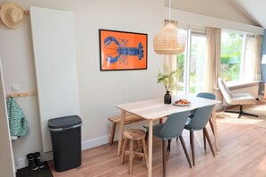 A dining area with a wooden table, blue chairs, a black trash bin, and a framed lobster picture on the wall. - Bungalow in Sint Maartenszee With Garden Views (Sint Maartensvlotbrug)
