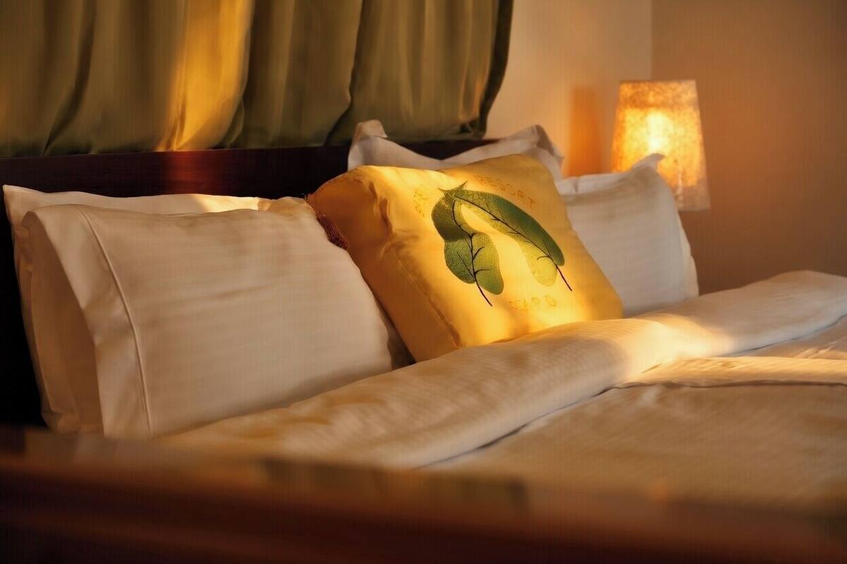 Una cama con ropa de cama blanca y una única almohada decorativa con un diseño de hoja.