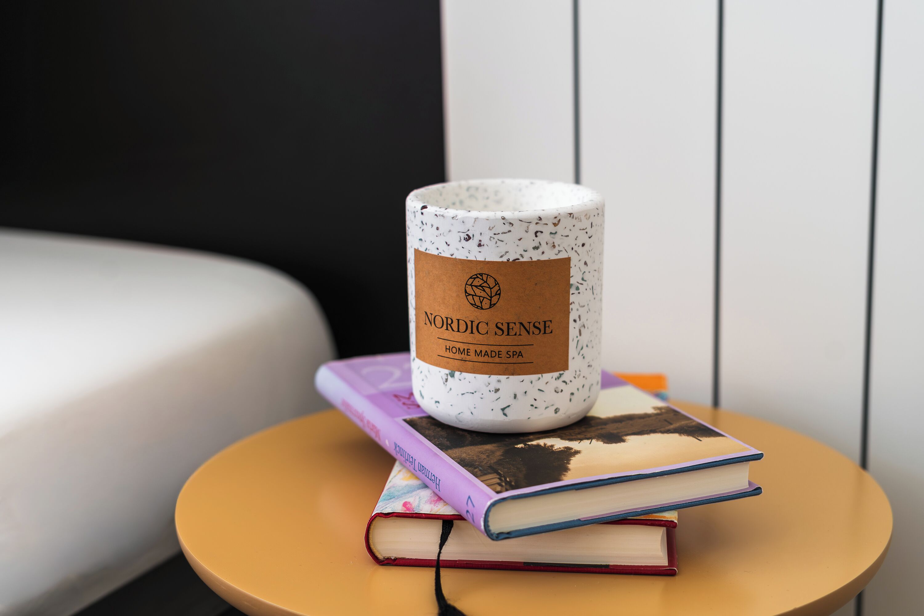 Una mesa redonda con una taza de cerámica blanca con el rótulo 'Nordic Sense Home Made Spa' y dos libros apilados encima.