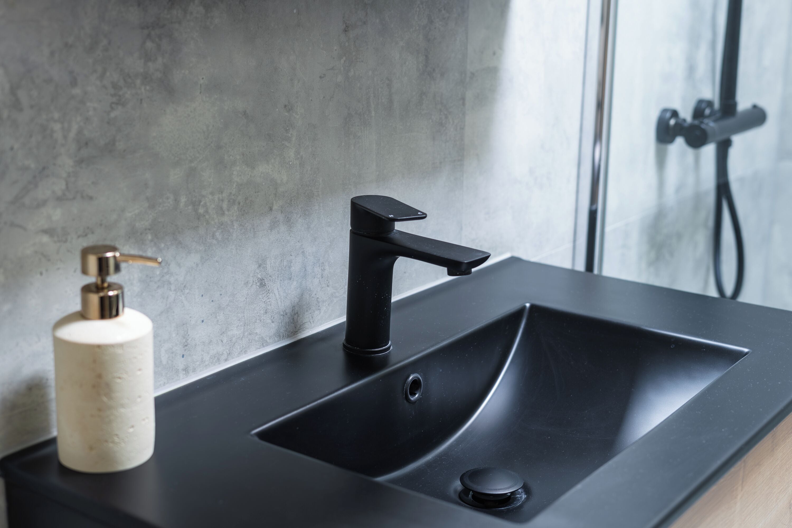 A bathroom with a black sink, a soap dispenser, and a shower area.