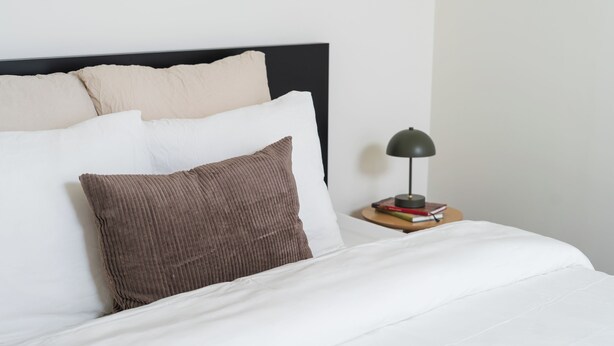 A neatly made bed with white and brown bedding, a black headboard, and a bedside table with a lamp and books. - Relaxing 2 Private Rooms Close to Center (Ghent)