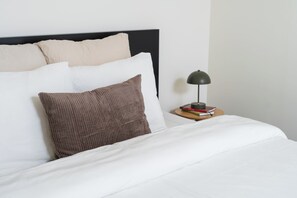 A neatly made bed with white and brown bedding, a black headboard, and a bedside table with a lamp and books. - Relaxing 2 Private Rooms Close to Center (Ghent)