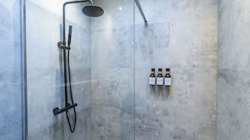 A shower area with a glass door, a handheld showerhead, and three bottles of shampoo on the wall.