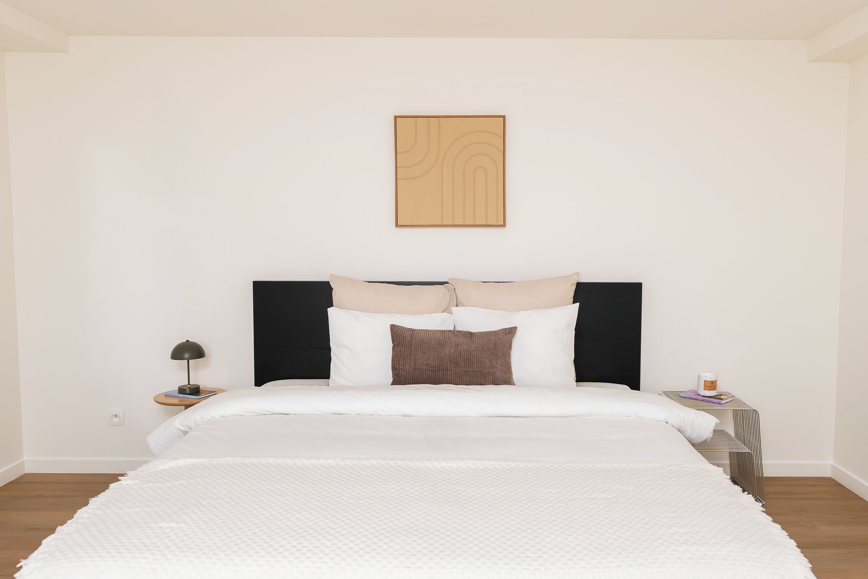 A neatly arranged bedroom with a bed, pillows, a bedside table with a lamp, and a small table with a cup.