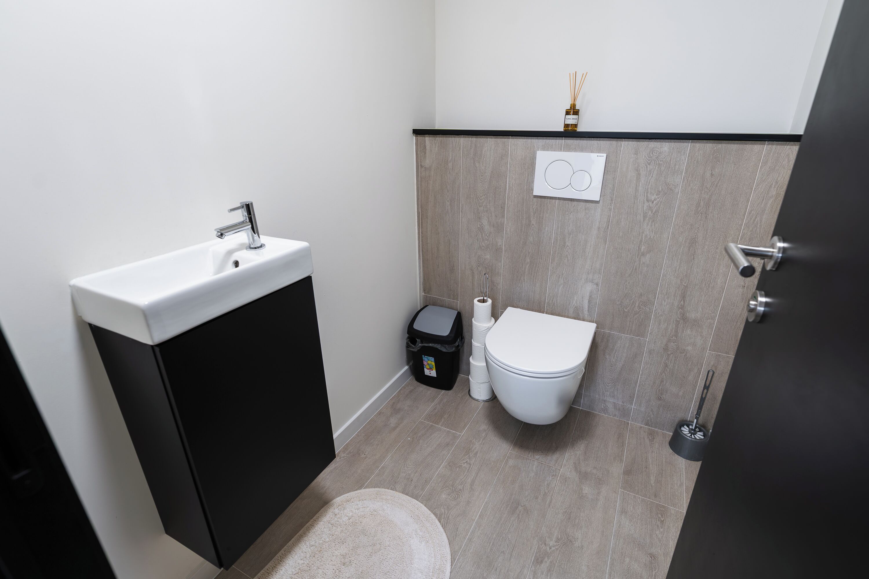 A bathroom with a white sink, black cabinet, toilet, and a towel rack.