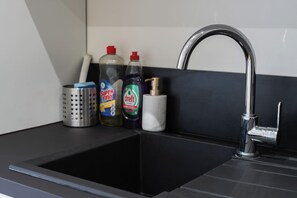Un lavamanos de cocina con grifo cromado, un colador de acero inoxidable y tres botellas de detergente para platos.
