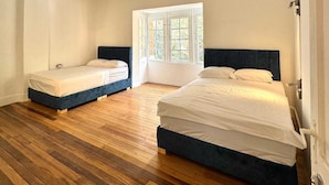 Ein Zimmer mit zwei Betten, einem großen Fenster, Holzboden und weißen Wänden.
