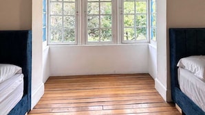 Ein Zimmer mit Holzboden, zwei Betten mit dunklen Kopfteilen und einem großen Fenster mit vielen Glasscheiben.