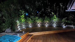 Une terrasse en bois dotée d’un espace salon incurvé, entourée de verdure et de murs en pierre.