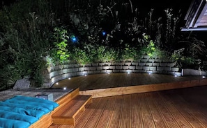 A wooden deck with a curved seating area, surrounded by greenery and stone walls.