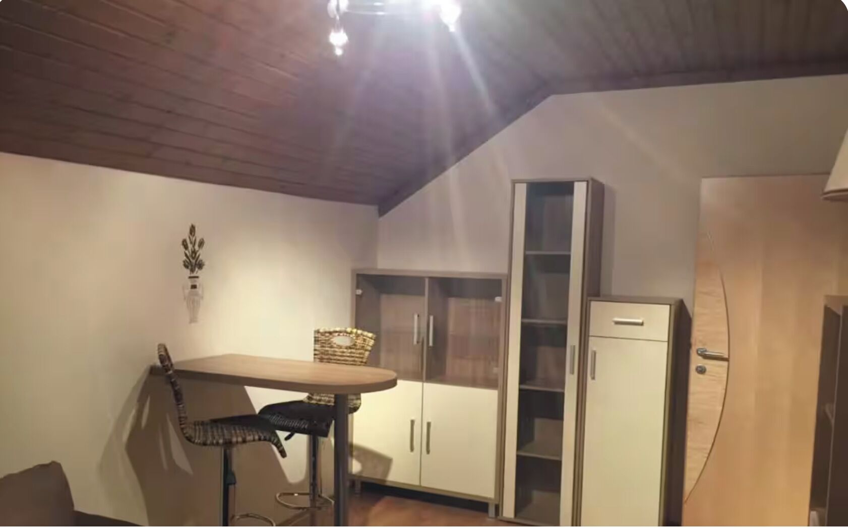 Une pièce avec un plafond en bois, une table à manger avec des chaises, un buffet aux portes vitrées et une armoire.