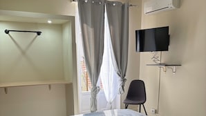 A bedroom with a bed, a TV, an air conditioner, a chair, and a window with curtains. - Rooms Duepuntozero  (Reggio Calabria)