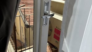 A view through a window with a metal door handle, a tiled balcony, and a sign with the word 'Haier'. - Rooms Duepuntozero  (Reggio Calabria)