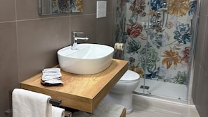 A modern bathroom with a wooden vanity, a white sink, a toilet, and a shower with floral curtains. - Rooms Duepuntozero  (Reggio Calabria)