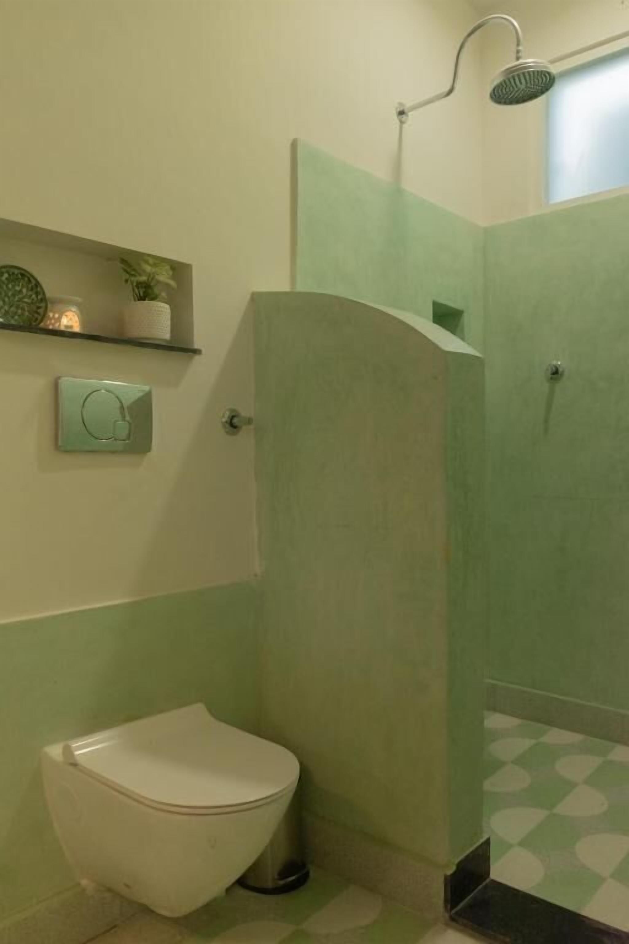 A bathroom with a toilet, a shower, and a green-tiled floor.