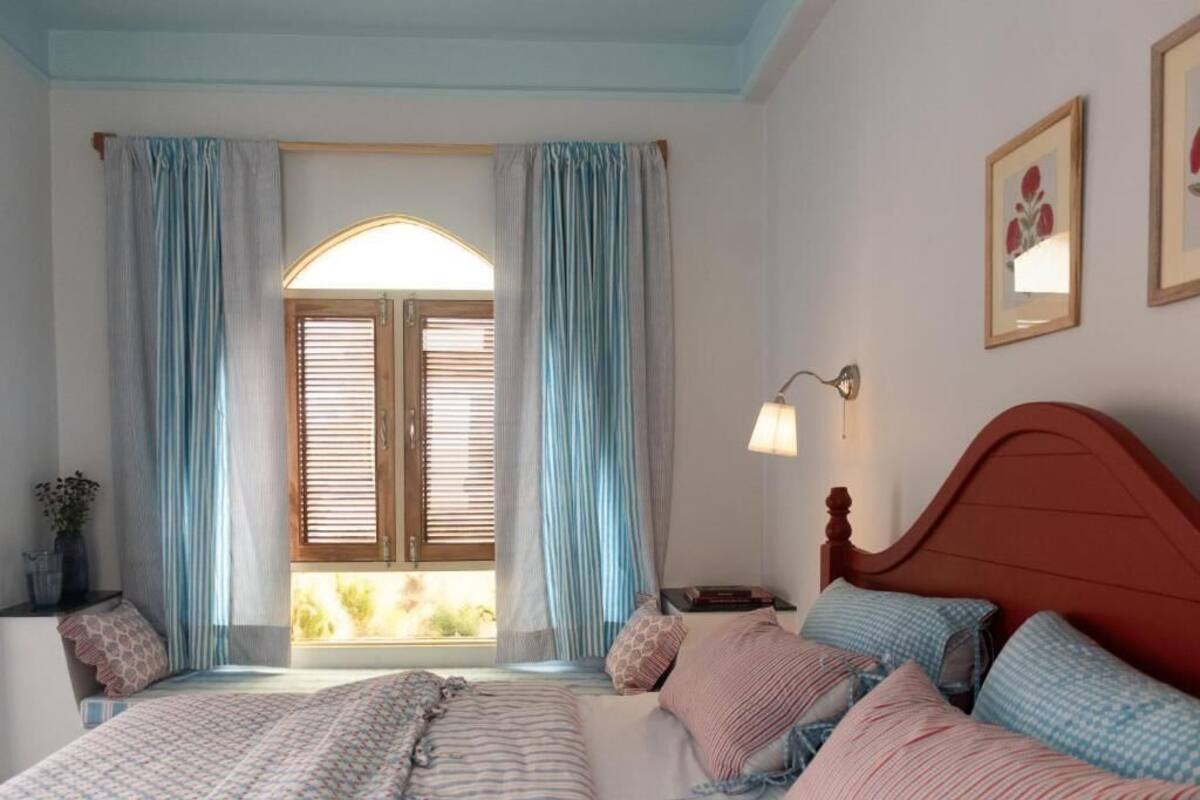 A bedroom with a bed, curtains, a window, a lamp, and a wall-mounted picture.