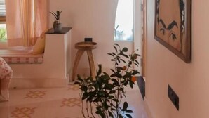 Una habitación con piso estampado, una planta en maceta, un cuadro en la pared y un ventanal con cortinas.
