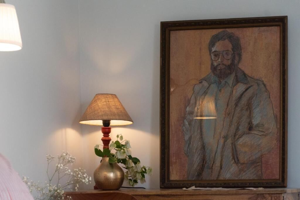 Ein gerahmtes Porträt an der Wand, eine Lampe mit einer Blumenvase und ein Holztisch.