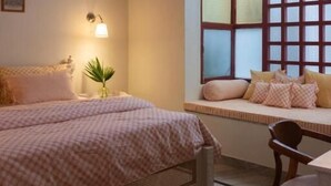 Un dormitorio con cama, mesita de noche, lámpara, ventana con persianas y una silla.